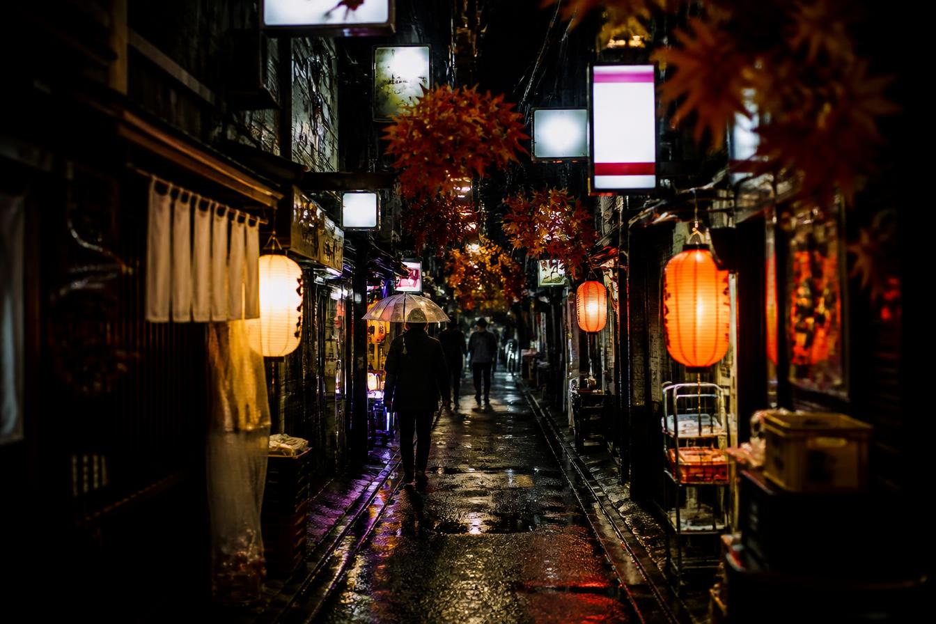 A narrow Tokyo alley of small bars glowing with lanterns on a wet night